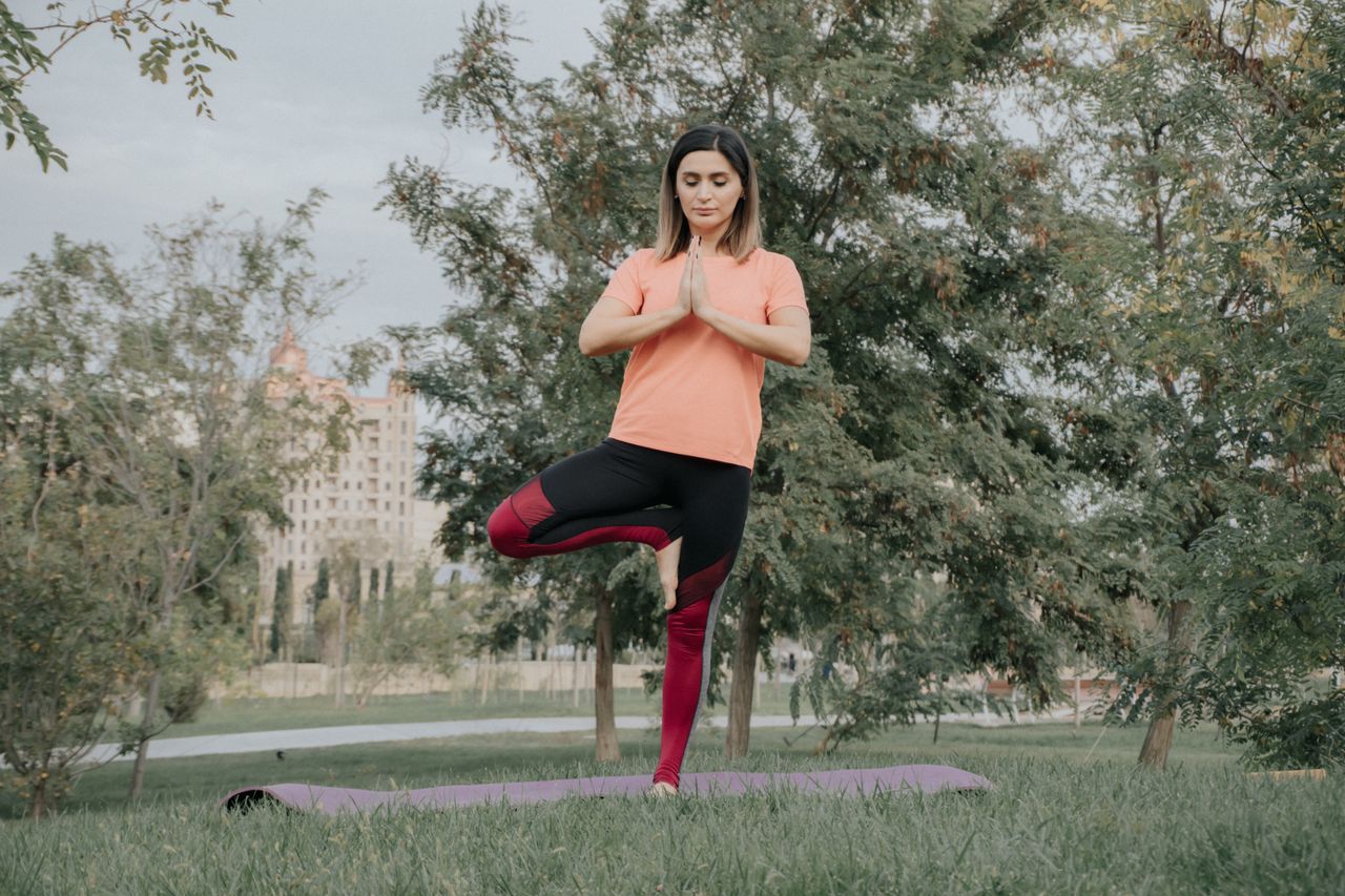 services-03 A woman in yoga pose outdoors on a mat in a park, showcasing balance and mindfulness.