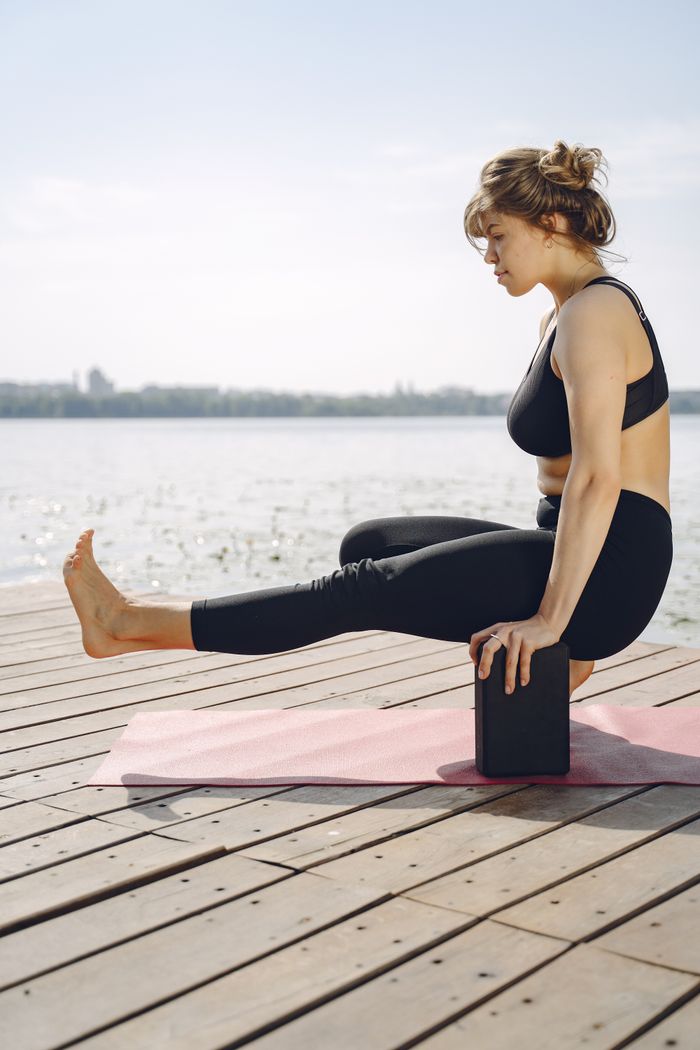Young woman in activewear doing yoga on a lakeside dock on a sunny day.