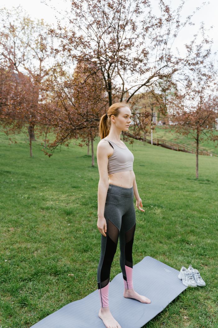 services-04 Young woman in activewear doing yoga exercises on a mat in a vibrant spring park setting.